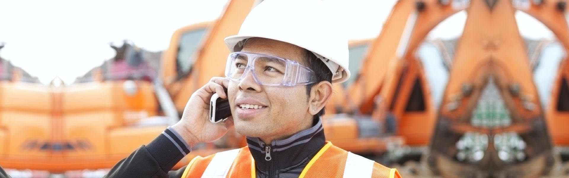 worker using mobilephone standing in front of excavator